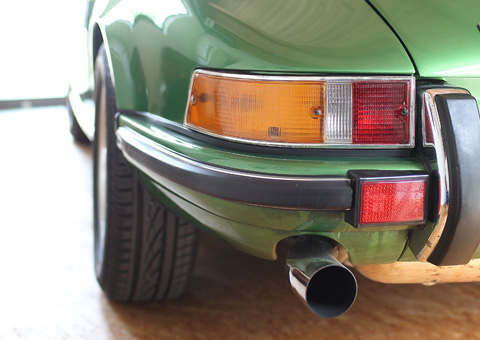 Heckdetail eines klassischen grünen Porsche 911 mit Rücklicht, Stoßstange und Chrom-Auspuffendrohr